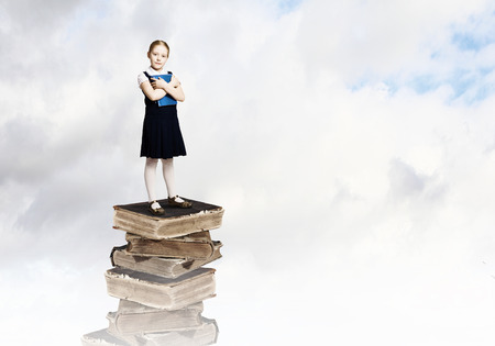 Image of cute school girl standing on pile of booksの写真素材