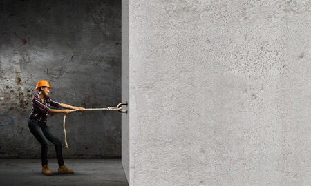 Image of woman in hardhat pulling cement wallの写真素材