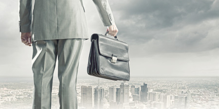 Back view of businessman with suitcase looking at cityの写真素材