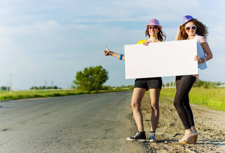 Two pretty young girls standing aside road with blank white bannerの写真素材