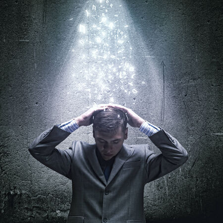 Businessman sitting under rain protecting head with armsの写真素材