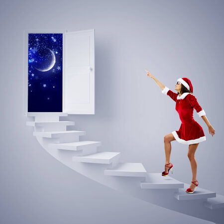Attractive young woman in Santa suit walking on ladderの写真素材