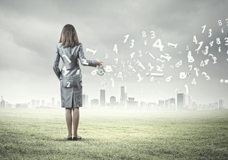 Back view of businesswoman holding alarm clock against city backgroundの写真素材