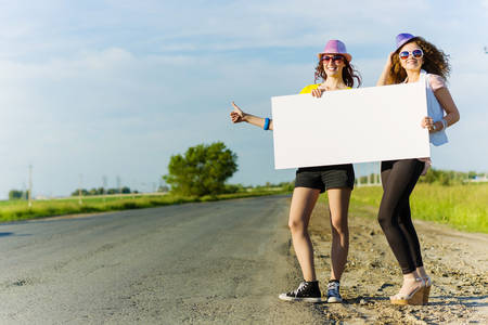 Two pretty young girls standing aside road with blank white bannerの写真素材
