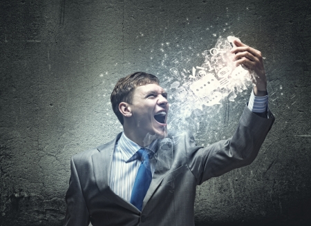 Angry businessman screaming into mobile phone furiouslyの写真素材
