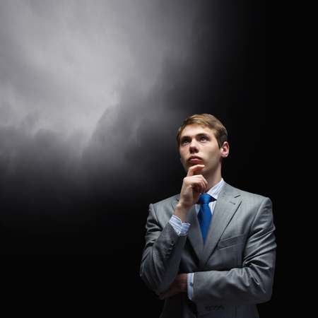 Young thoughtful businessman looking up with hand on chinの写真素材