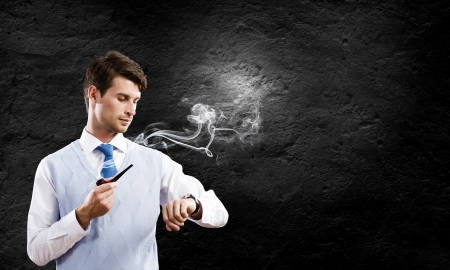 Young handsome businessman smoking pipe against black backgroundの写真素材
