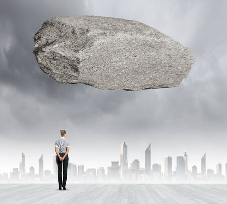 Rear view of businesswoman looking at urban scene with huge stone aboveの写真素材