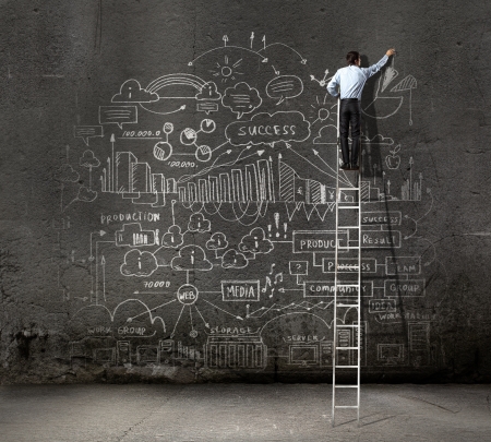 Rear view of businessman standing on ladder and drawing business sketch on wallの写真素材