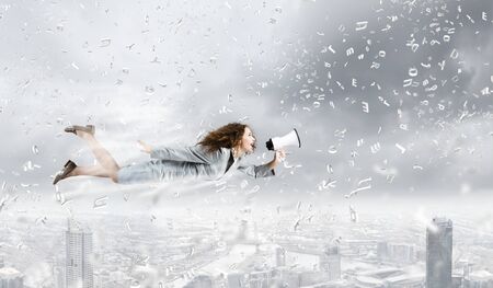 Young pretty businesswoman flying in blue sky sreaming in megaphoneの写真素材