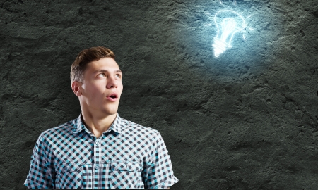 Young man and electrical bulb against dark backgroundの写真素材