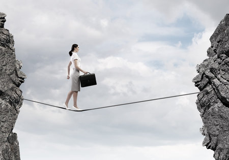 Young confident businesswoman walking on rope above gapの写真素材