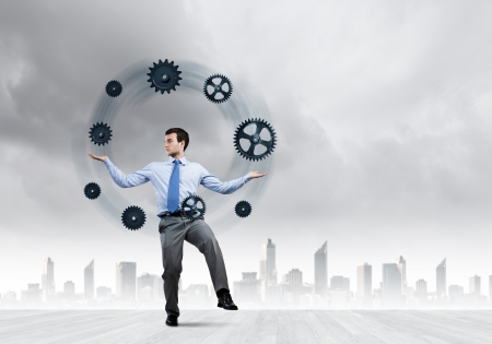 Handsome businessman juggling with gears against city backgroundの写真素材