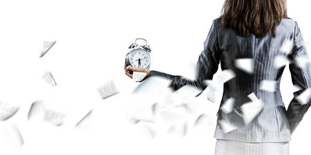 Back view of businesswoman holding alarm clock against white backgroundの写真素材
