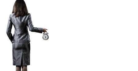 Back view of businesswoman holding alarm clock against white backgroundの写真素材