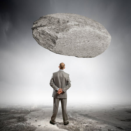 Rear view of confident businessman with huge stone aboveの写真素材