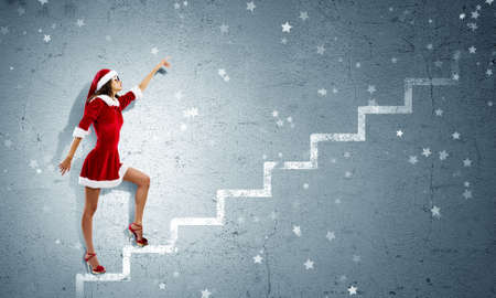 Attractive young woman in Santa suit walking on ladderの写真素材