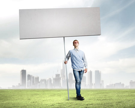 Young man against city background holding blank banner  Place for textの写真素材