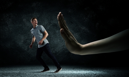 Funny image of young man trying to escape from huge handの写真素材