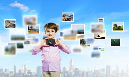 Image of cute boy holding photo camera standing among photosの写真素材