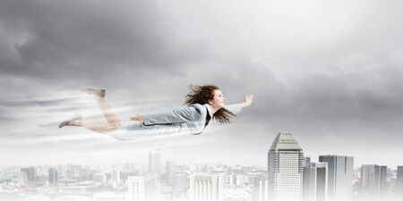 Young pretty businesswoman flying in sky above cityの写真素材