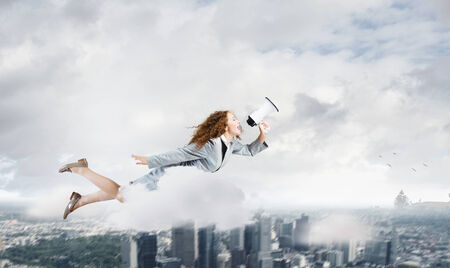 Young pretty businesswoman flying in blue sky sreaming in megaphoneの写真素材
