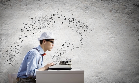 Young funny man in glasses writing on typewriterの写真素材