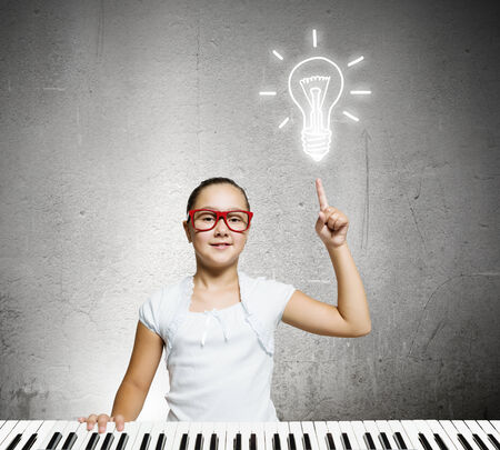 Pretty school girl in funny glasses playing pianoの写真素材