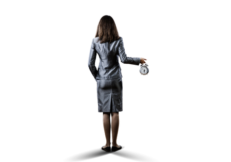 Back view of businesswoman holding alarm clock against white backgroundの写真素材