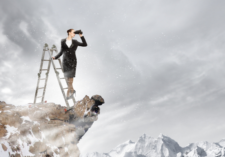 Image of businesswoman standing on ladder and looking in binocularsの写真素材