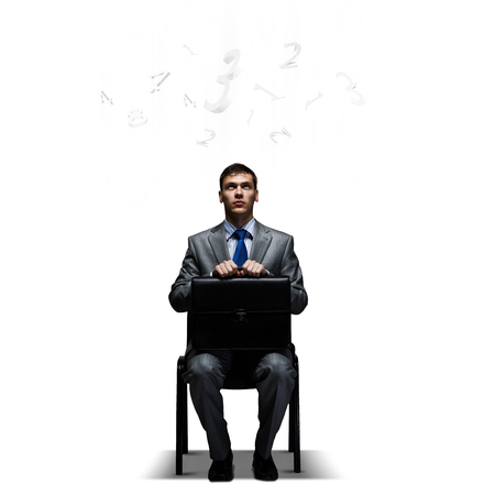 Young businessman sitting on chair with suitcase on kneesの写真素材