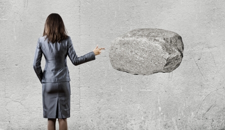 Businesswoman pointing with finger at huge stoneの写真素材