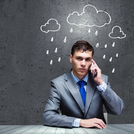 Businessman sitting under rain talking on mobile phoneの写真素材