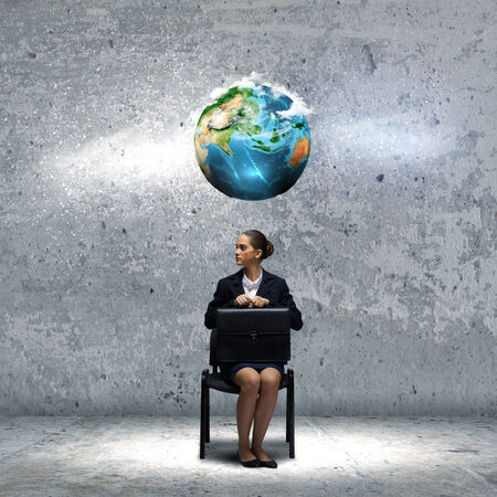 Young upset businesswoman with suitcase sitting on chair  Elements of this image are furnished by NASAの写真素材