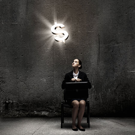 Young businesswoman sitting on chair and looking at dollar symbol aboveの写真素材