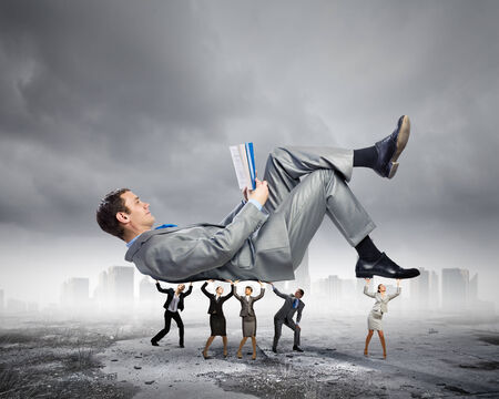 Young businessman lying and reading book supported by colleaguesの写真素材