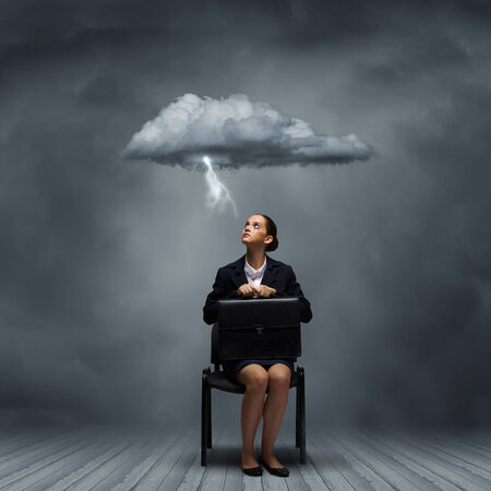 Young upset businesswoman with suitcase sitting on chairの写真素材