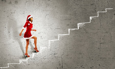 Attractive young woman in Santa suit walking on ladderの写真素材