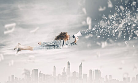 Young pretty businesswoman flying in blue sky sreaming in megaphoneの写真素材