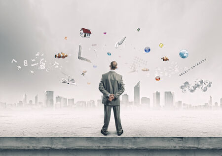 Back view of confident businessman looking at city with items flying in airの写真素材