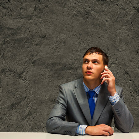 Businessman sitting under rain talking on mobile phoneの写真素材