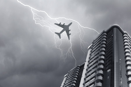 Bottom view of airplane flying above skyscraper in stormy skyの写真素材