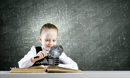 Schoolgirl examining opened book with magnifying glass