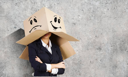 Businesswoman wearing carton box with drawn smiley on headの写真素材