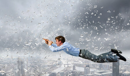 Young businessman flying in sky and playing fifeの写真素材