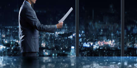 Businessman standing against office window reading documentsの写真素材