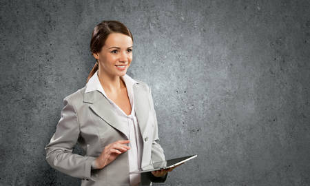 Young pretty businesswoman against grey background using tablet pcの写真素材