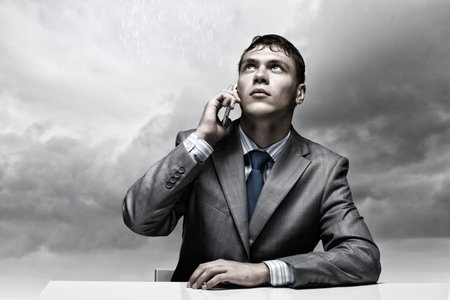 Businessman sitting under rain talking on mobile phoneの写真素材