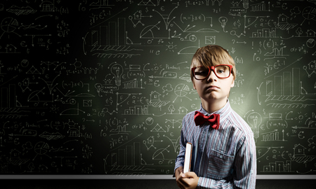 Genius boy in red glasses near blackboard with formulasの写真素材
