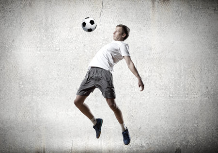 Football player kicking ball against cement backgroundの写真素材